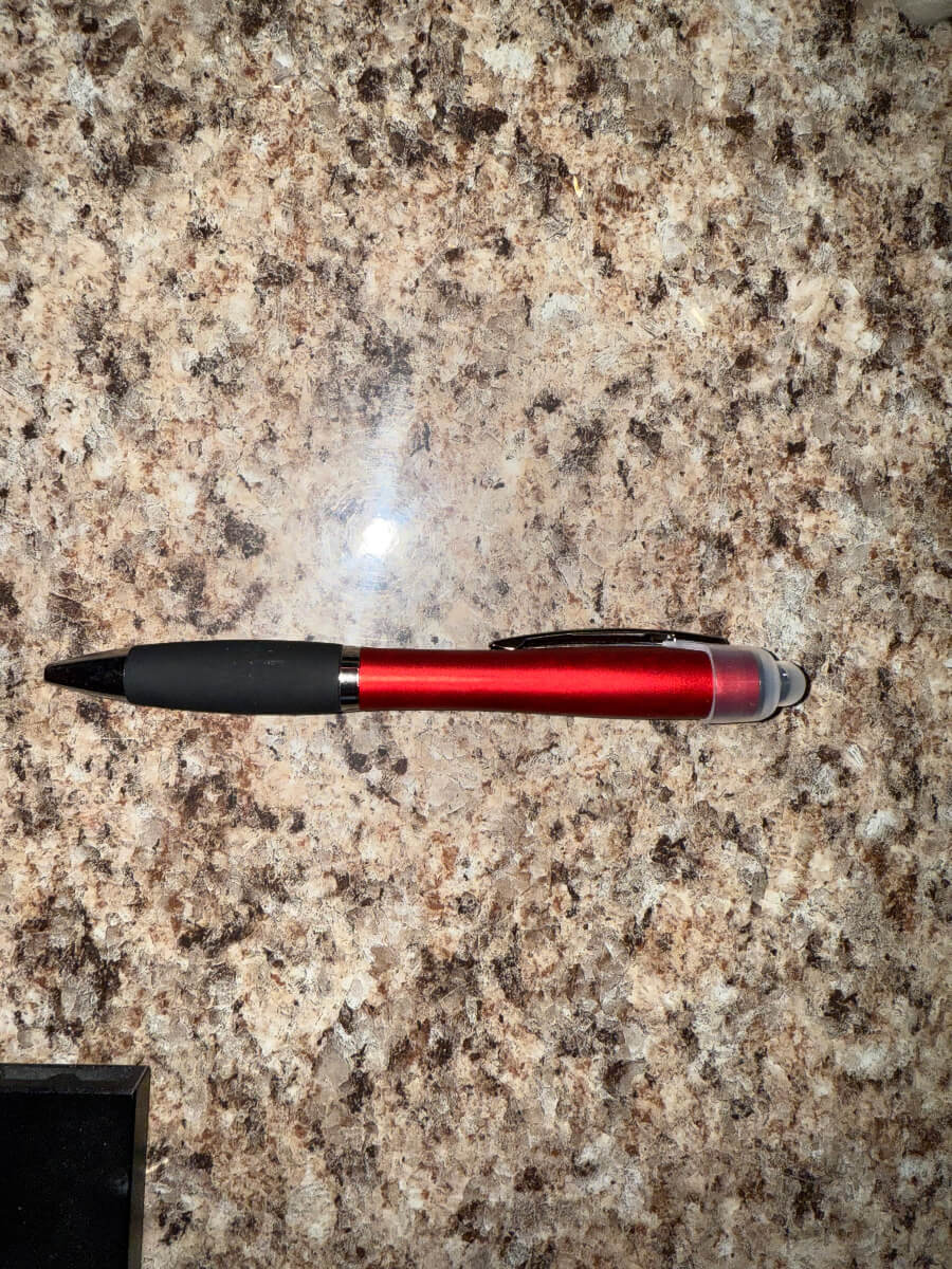 Red 3-in-1 stylus pen with black grip, LED light tip, and ballpoint, ideal for custom engraving and promotional gifts, displayed on a granite surface