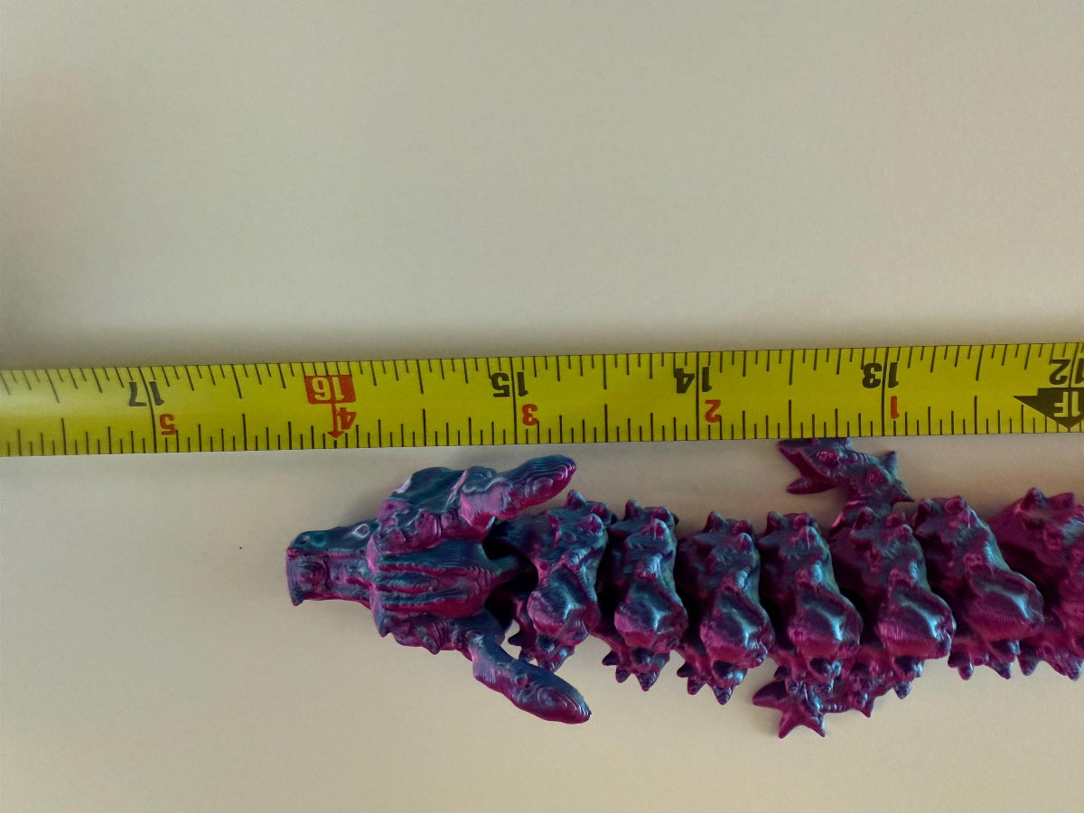 3D printed articulated dragon in purple and blue shown with measuring tape for size reference